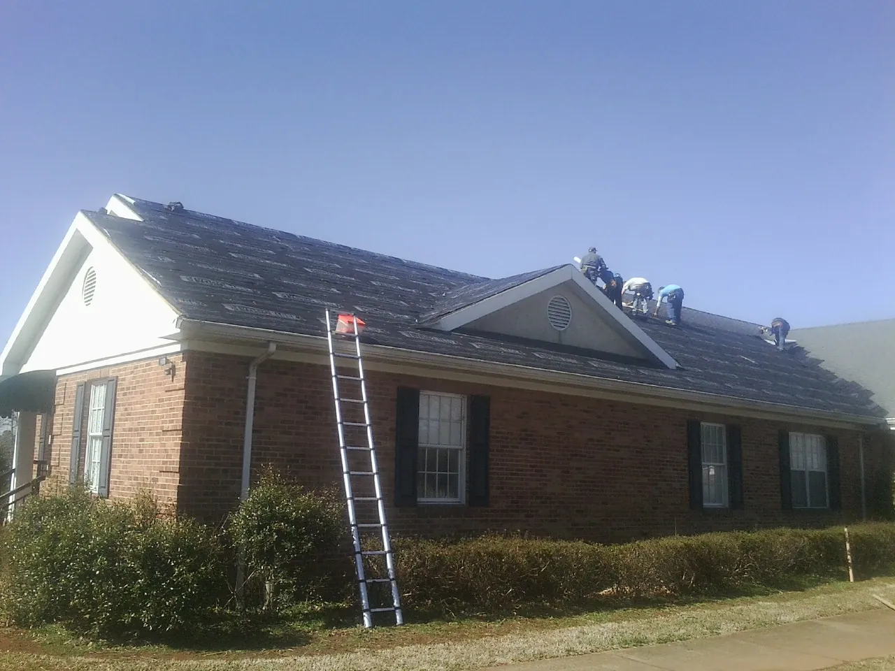 Crew tearing shingles off a brick ranch roof with a ladder set — Metal Roof Repair work by our crew in Spring Gap