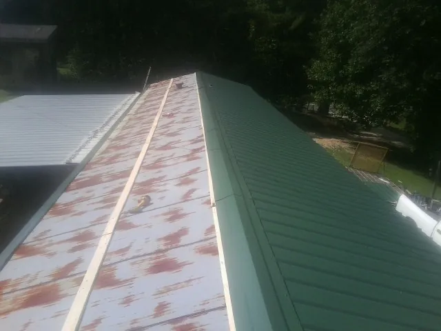Old rusted panels beside newly installed green metal roofing — Wind Damage Roof Repair by Roofing Brothers in Spring Gap
