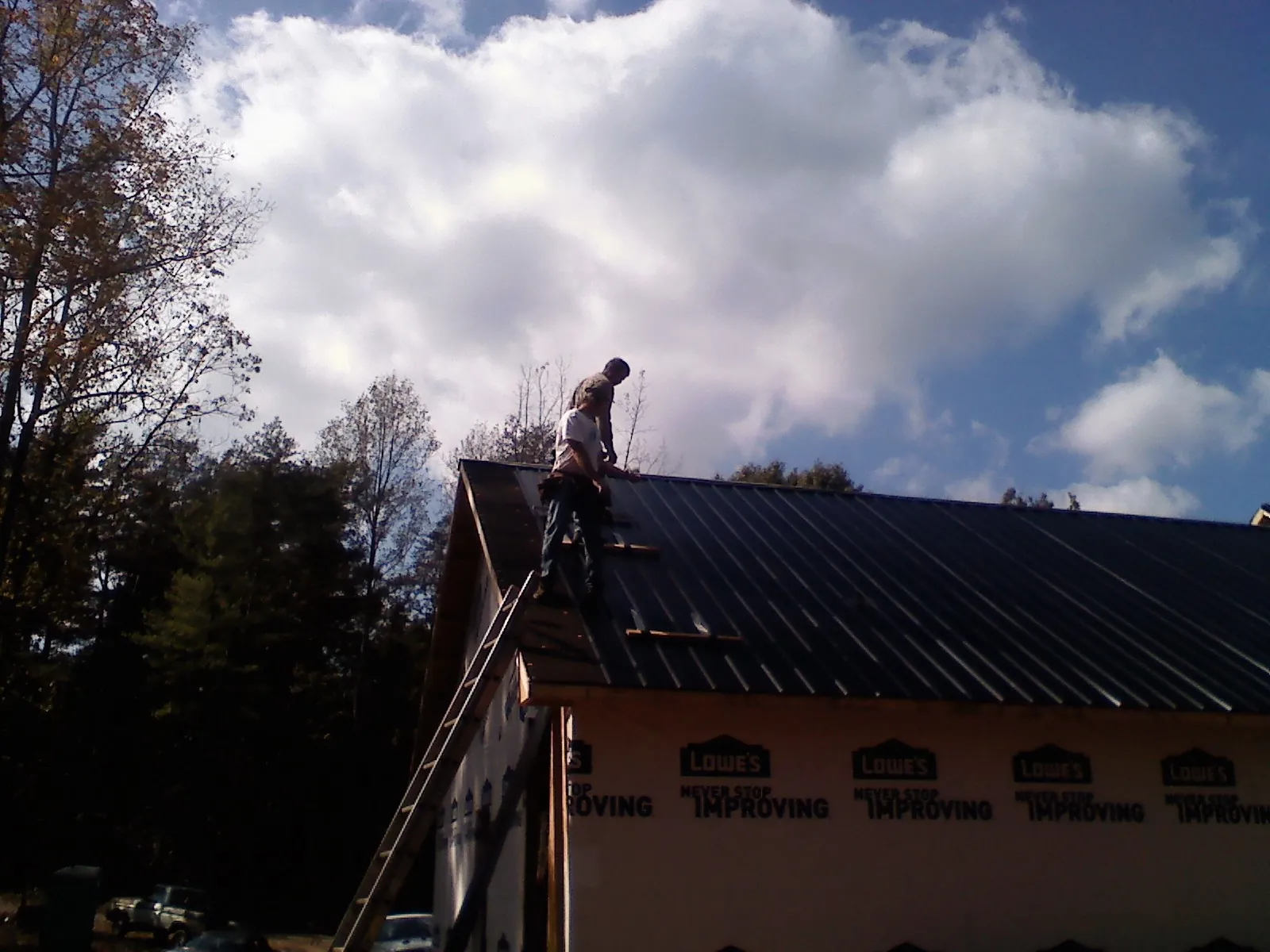 Roofer fastening dark metal panels high against a cloudy sky, from a Roof Inspection job in Spring Gap