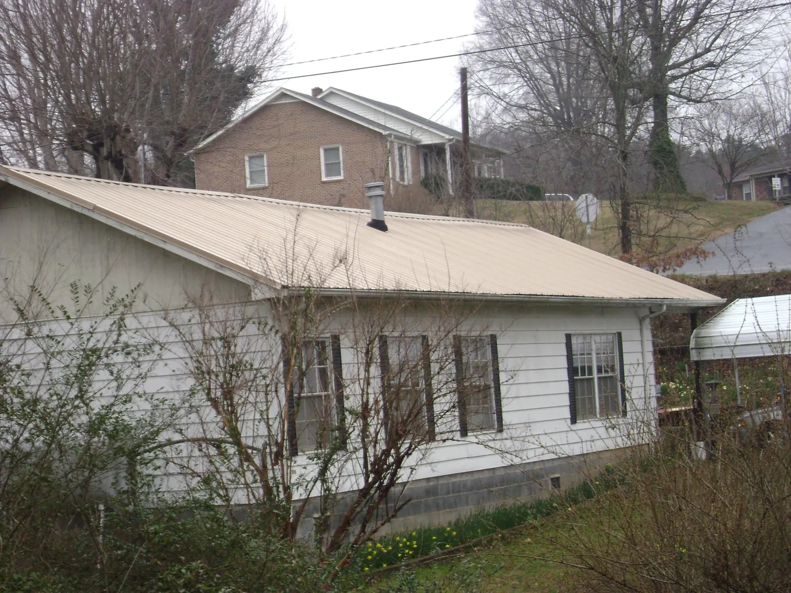 Tan metal roof on a white sided house set into a hillside — Commercial Roofing by Roofing Brothers in Spring Gap